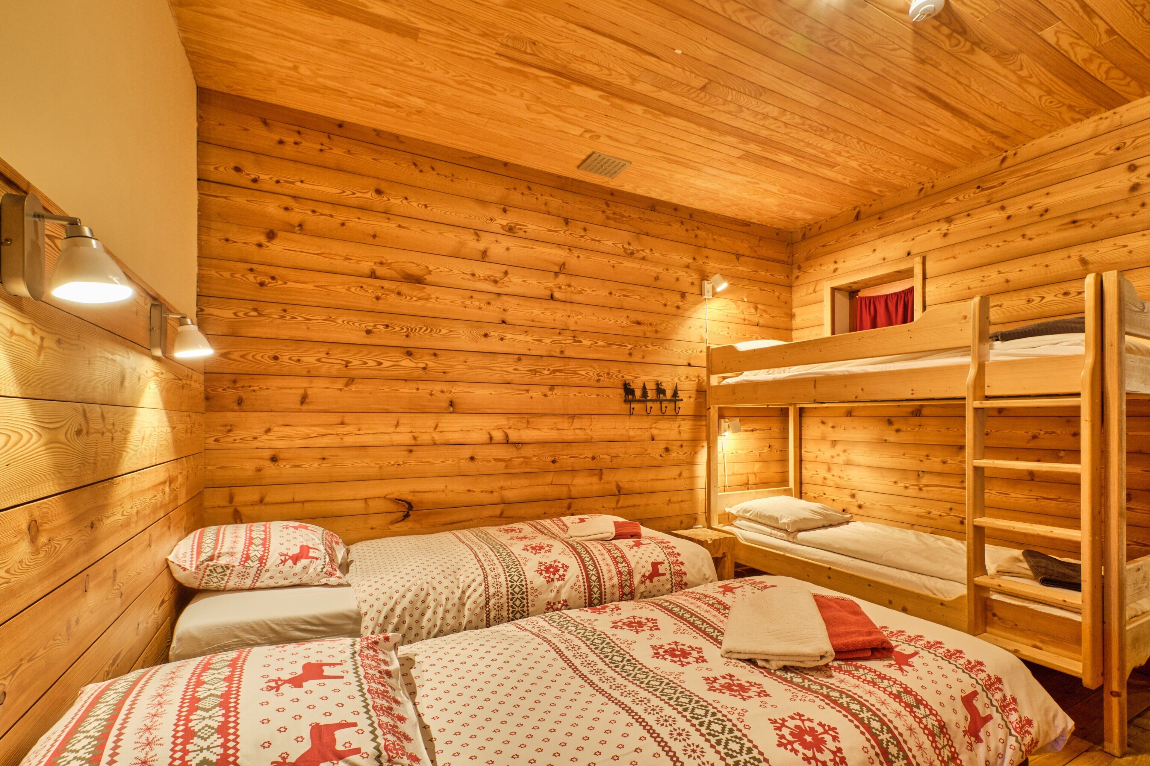 A wooden cabin room with bunk beds, two bedside tables, and wall-mounted lights.