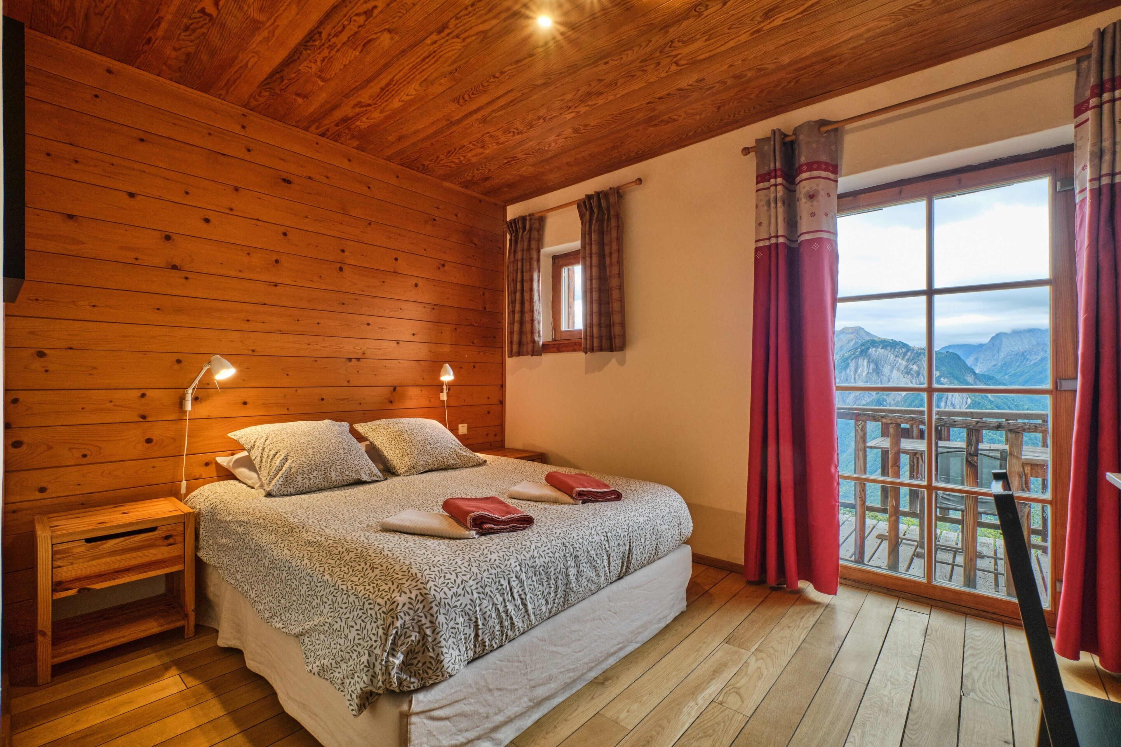 Una habitación con paneles de madera, una cama, una mesita de noche y un ventanal con cortinas.