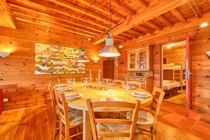 Ein Interieur einer Holzhütte mit einem Esstisch für sechs Personen, Holzwänden und einem Bett im Hintergrund.