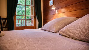 Un lit avec une literie à motifs, une fenêtre avec des rideaux, un mur en bois et un petit cadre photo.