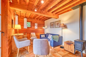 Un intérieur chaleureux, avec des murs en bois, un canapé, des fauteuils, une table et un poêle à bois.