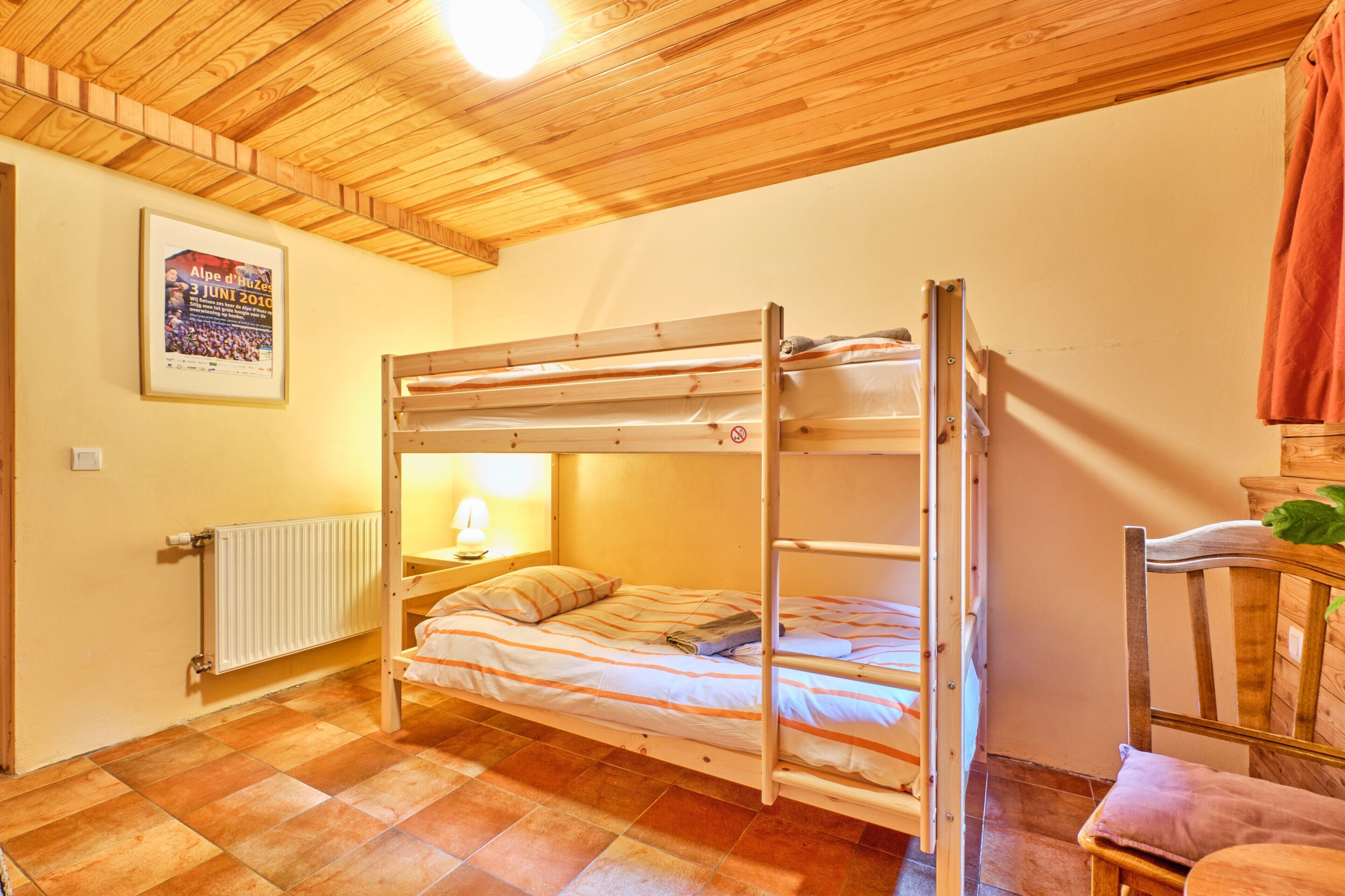 Una cama litera en una habitación con techo y paredes de madera, un radiador, un cartel en la pared y una silla.