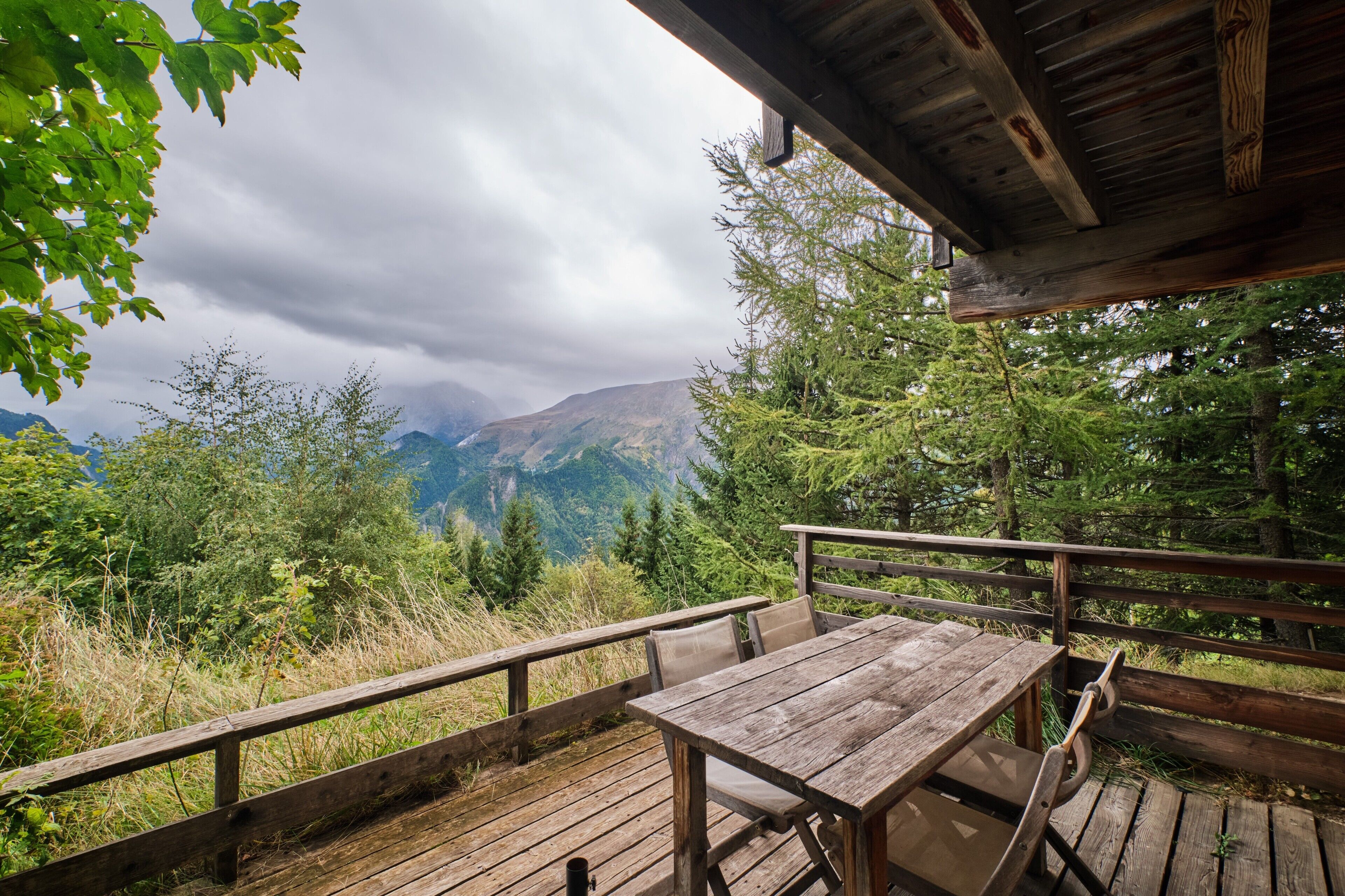 Une terrasse en bois avec une table et des chaises, offrant une vue sur un paysage montagneux.