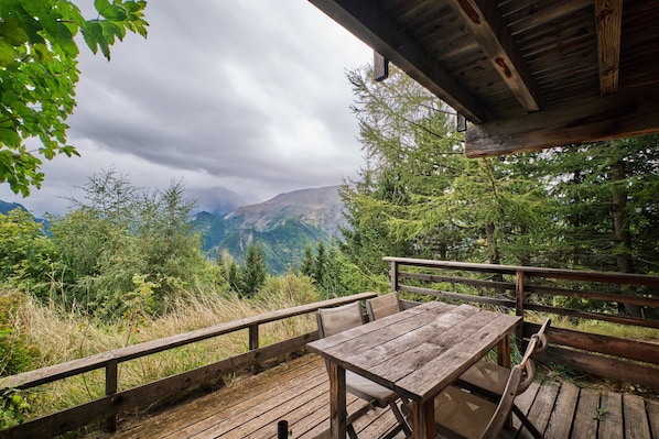 A wooden deck with a table and chairs, overlooking a mountainous landscape.