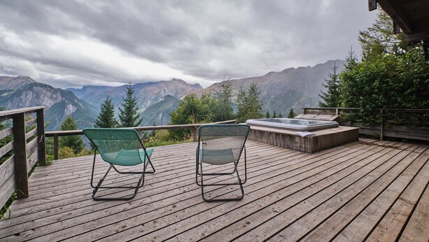 A wooden deck with two green chairs and a hot tub overlooking a mountainous landscape. - Chalet 'Il Fera Beau Demain' with Mountain View, Private Terrace and Wi-Fi (Villard-Reculas)