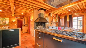 A kitchen with wooden beams, a stove, and a dining area with a table and chairs. - Chalet 'Il Fera Beau Demain' with Mountain View, Private Terrace and Wi-Fi (Villard-Reculas)