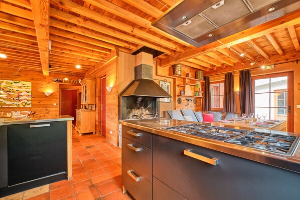 A kitchen with wooden beams, a stove, and a dining area with a table and chairs. - Chalet 'Il Fera Beau Demain' with Mountain View, Private Terrace and Wi-Fi (Villard-Reculas)