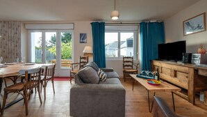 Een woonkamer met een bank, eettafel, stoelen, een televisie en een keukenhoek.