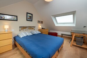 Une chambre à coucher comprenant un lit, des tables de chevet, un bureau, une fenêtre et des œuvres d’art accrochées aux murs.