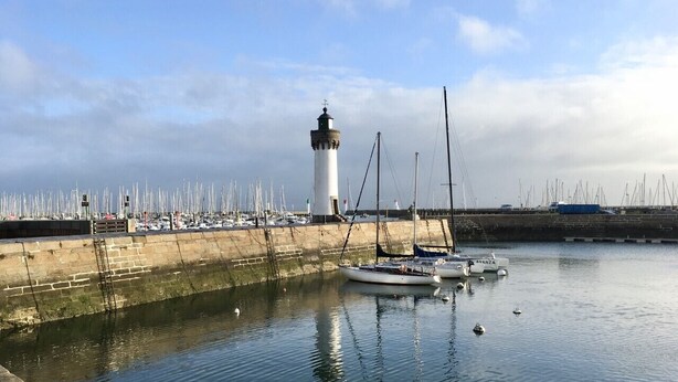 Een haven met een vuurtoren, boten en een jachthaven met talloze zeilboten.