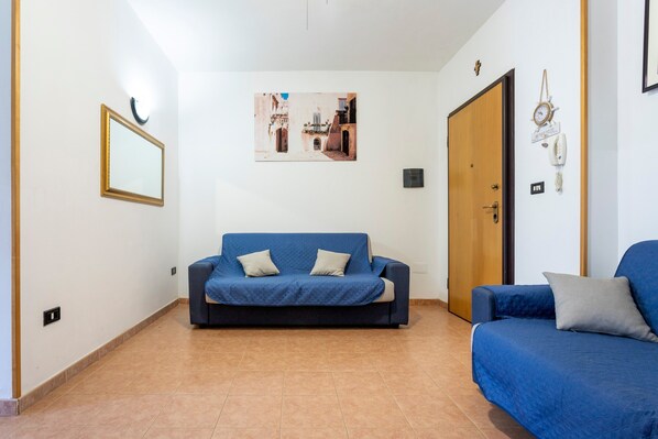 Una habitación con un sofá azul, una puerta de madera, un cuadro en la pared y un interruptor de luz.