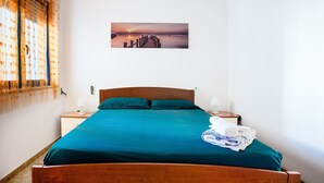 A neatly made bed with a teal bedspread, a wooden headboard, and a folded towel on the side.