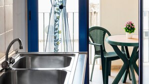 A kitchen with a double sink, a green chair, and a small table with a potted plant.