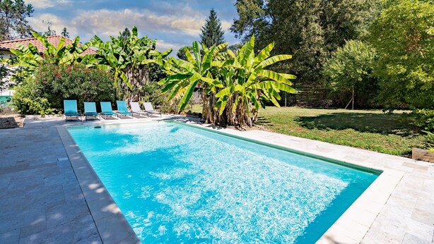 Una piscina con acqua cristallina circondata da una terrazza con lettini e un prato.