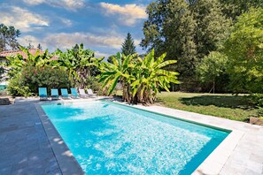 Una piscina con agua azul cristalina, rodeada por una zona de patio con sillas de descanso y un césped.