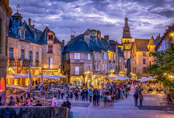 Una plaza animada con edificios históricos, mesas al aire libre y una multitud de gente.