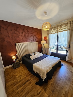 Ein Schlafzimmer mit einem Bett, einer Nachttischlampe, einem Heizkörper und einem Fenster mit Vorhängen.