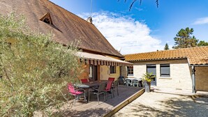 Una casa con tetto in tegole, un patio con tavolo e sedie e un piccolo giardino.
