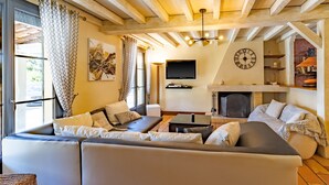 Un soggiorno con un divano componibile, una TV a schermo piatto, un camino e una sveglia appesa al muro.