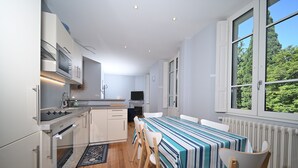 A modern kitchen with white cabinets, a stove, and a dining area with a striped tablecloth. - Le Clos du Casino, T3 "Le Céciré" for 4 to 6 guests (Bagnères de Luchon)