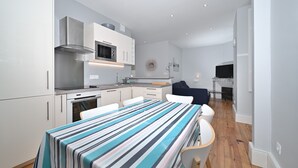A modern kitchen with white cabinets, stainless steel appliances, and a striped tablecloth-covered dining table. - Le Clos du Casino, T3 "Le Céciré" for 4 to 6 guests (Bagnères de Luchon)