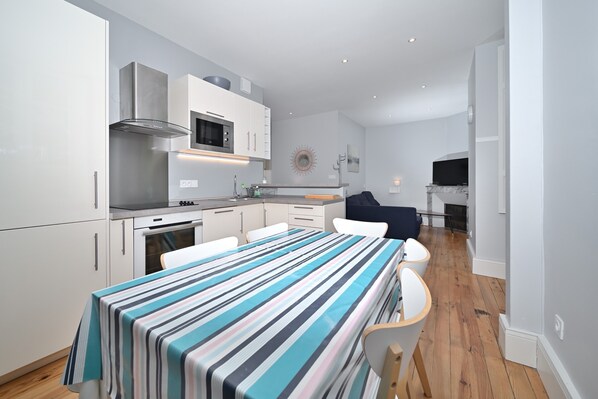 Une cuisine moderne avec des meubles blancs, des appareils en acier inoxydable et une table à manger recouverte d’une nappe à rayures.