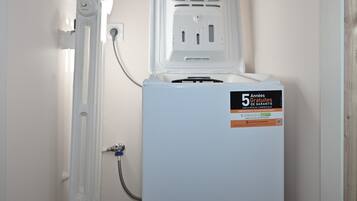 Il s’agit d’un appareil électroménager blanc, muni d’une étiquette indiquant une garantie de cinq ans. Il est fixé au mur, avec une prise électrique visible et un tuyau qui y est raccordé.