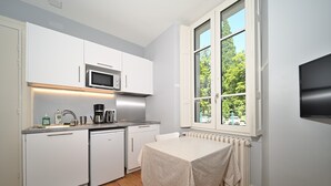 Eine kleine Küche mit weißen Schränken, einer Mikrowelle, einer Kaffeemaschine und einem Tisch mit Tischdecke.