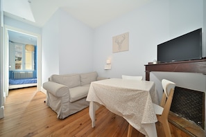 A room with a sofa, a table, a television, and a fireplace.