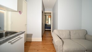 A modern kitchen with a stainless steel sink, a white cabinet, and a beige sofa in a hallway.
