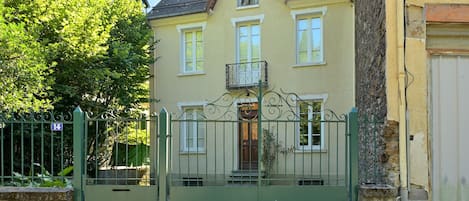 Una casa de dos pisos con un balcón, un portón verde y un cartel con el número 14.