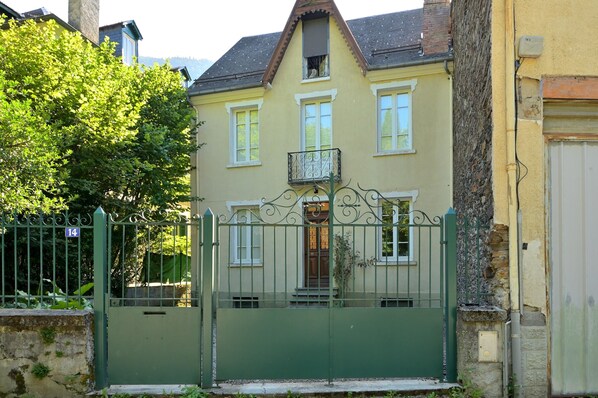 A two-story house with a balcony, a green gate, and a number 14 sign.