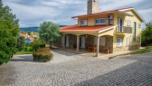 A two-story house with a stone facade, a red-tiled roof, and a balcony.