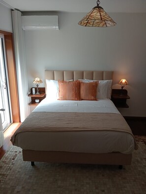 A neatly made bed with a headboard, two bedside tables with lamps, and a large window with curtains.