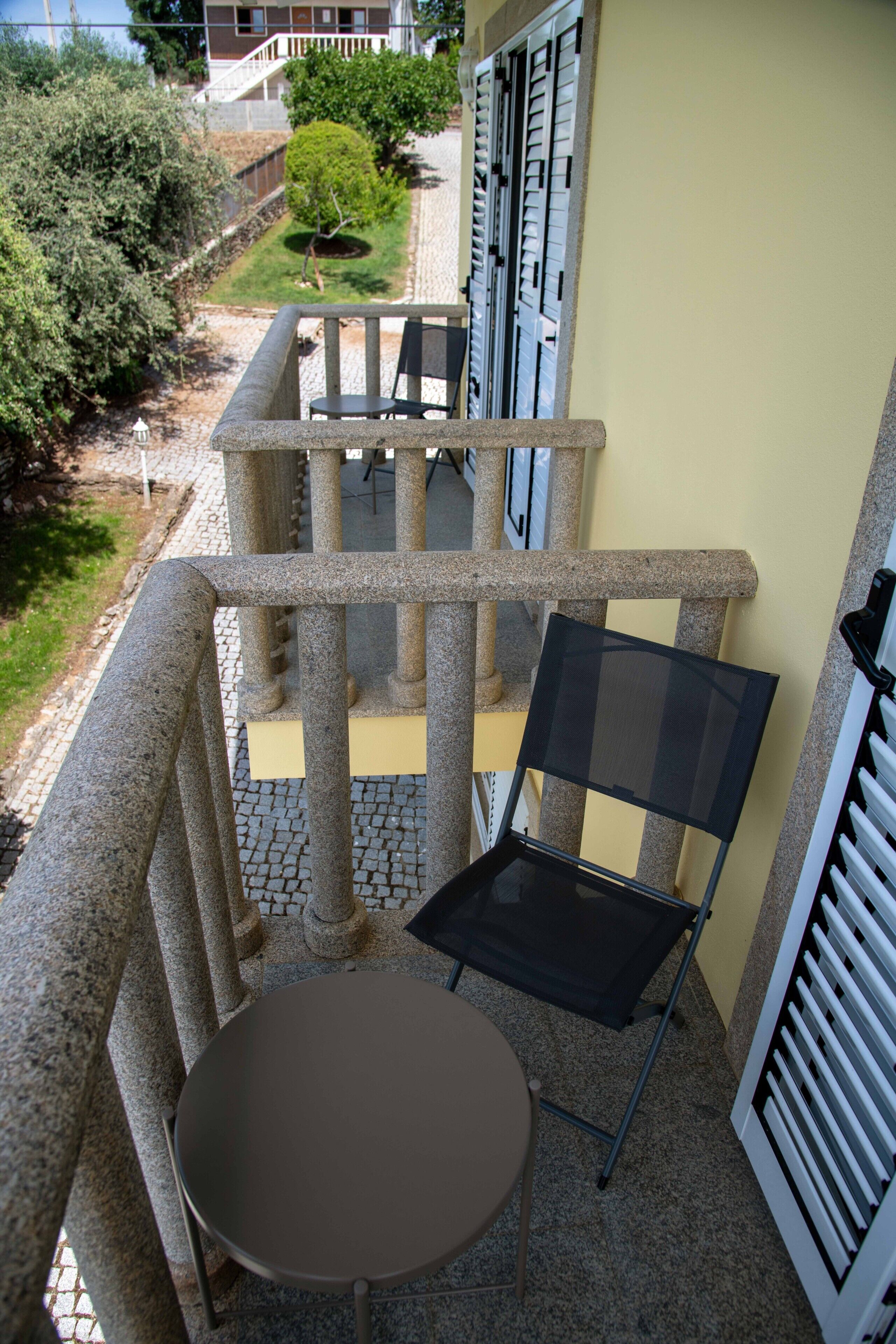 Een balkon met een tafel en stoelen, een kleine tuin en een gebouw op de achtergrond.