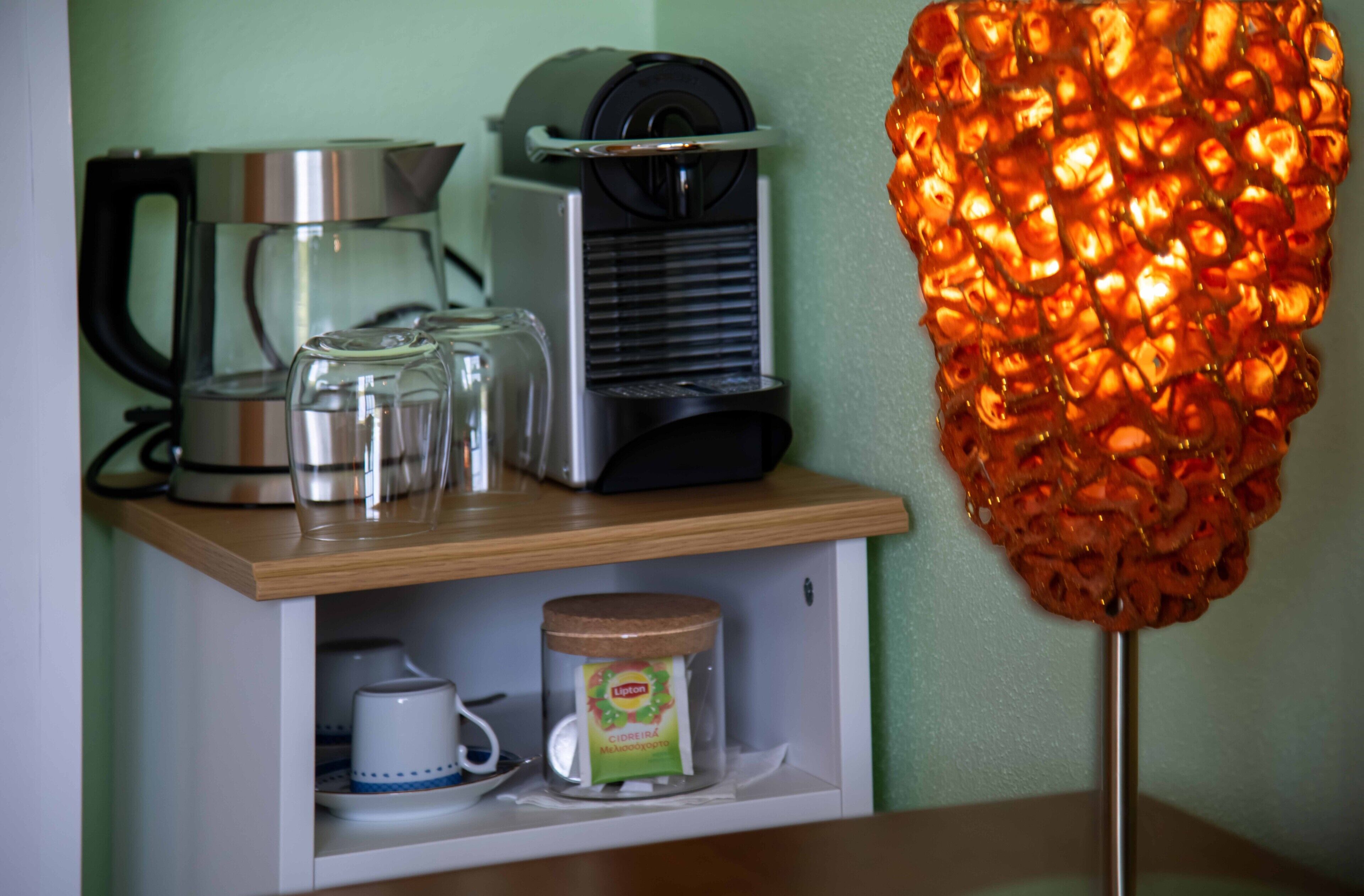 A kitchen area with a coffee maker, a kettle, a glass jar, and a decorative orange light fixture.