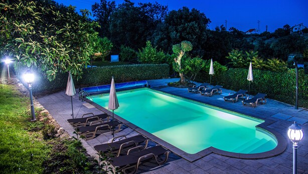A swimming pool with lounge chairs and umbrellas, surrounded by greenery.