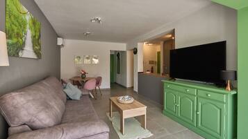 Una sala de estar con un sofá, una mesa de centro, un televisor y una cocina con un mueble verde.