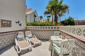 Eine Terrasse mit zwei Lounge-Sesseln und einem Tisch, umgeben von dekorativen Fliesen und Blick auf ein Gebäude sowie Palmen.
