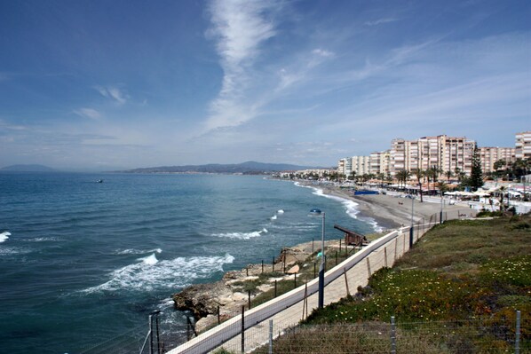 A coastal view with a beach, ocean waves, a fence, and buildings in the background. - Apartment 'Casita Helena' with Sea View, Wi-Fi and Air Conditioning (Torrox)