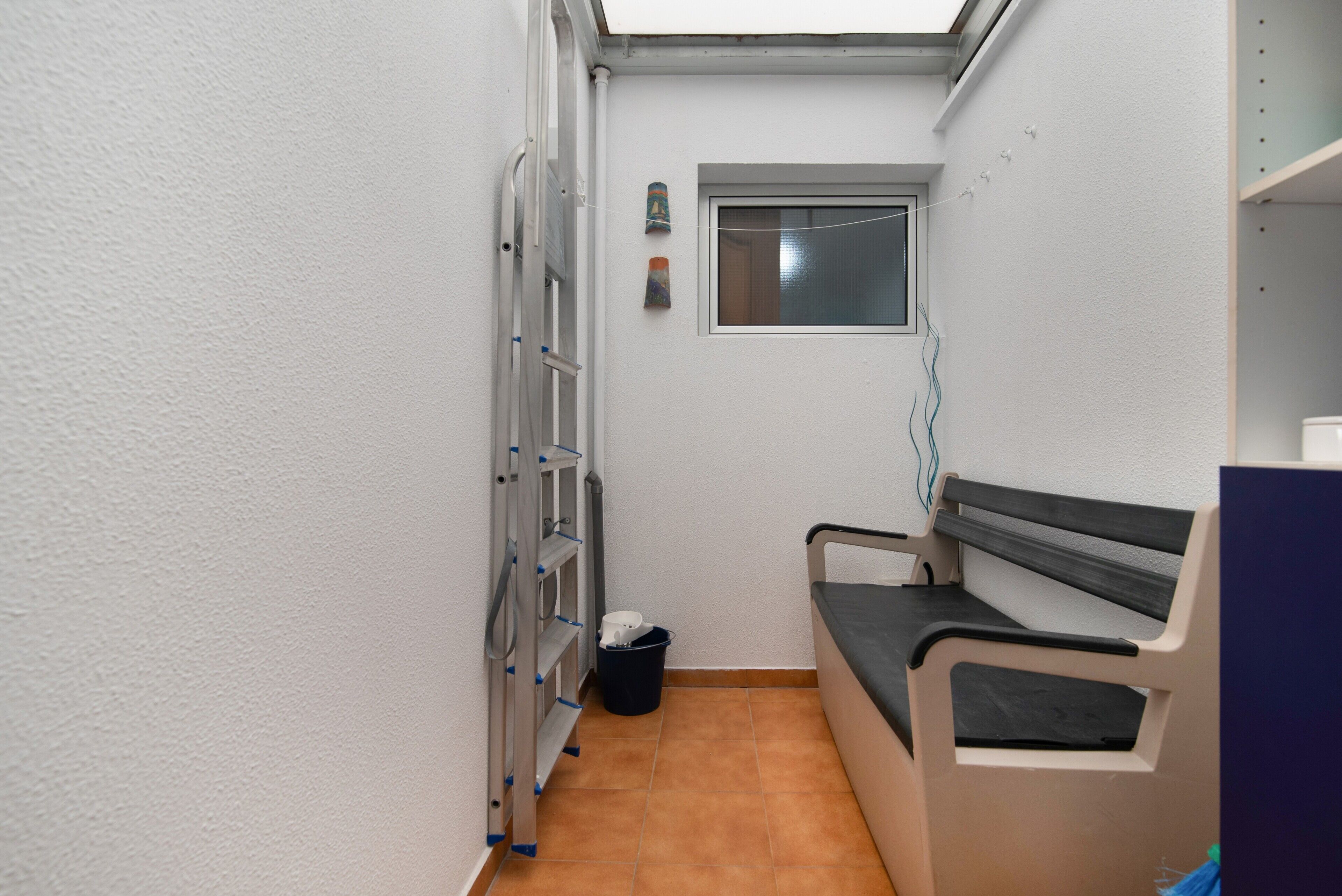Een smalle kamer met een bankje, een raam en een wandplank.