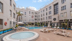 A hotel courtyard with a swimming pool, lounge chairs, and a hot tub.