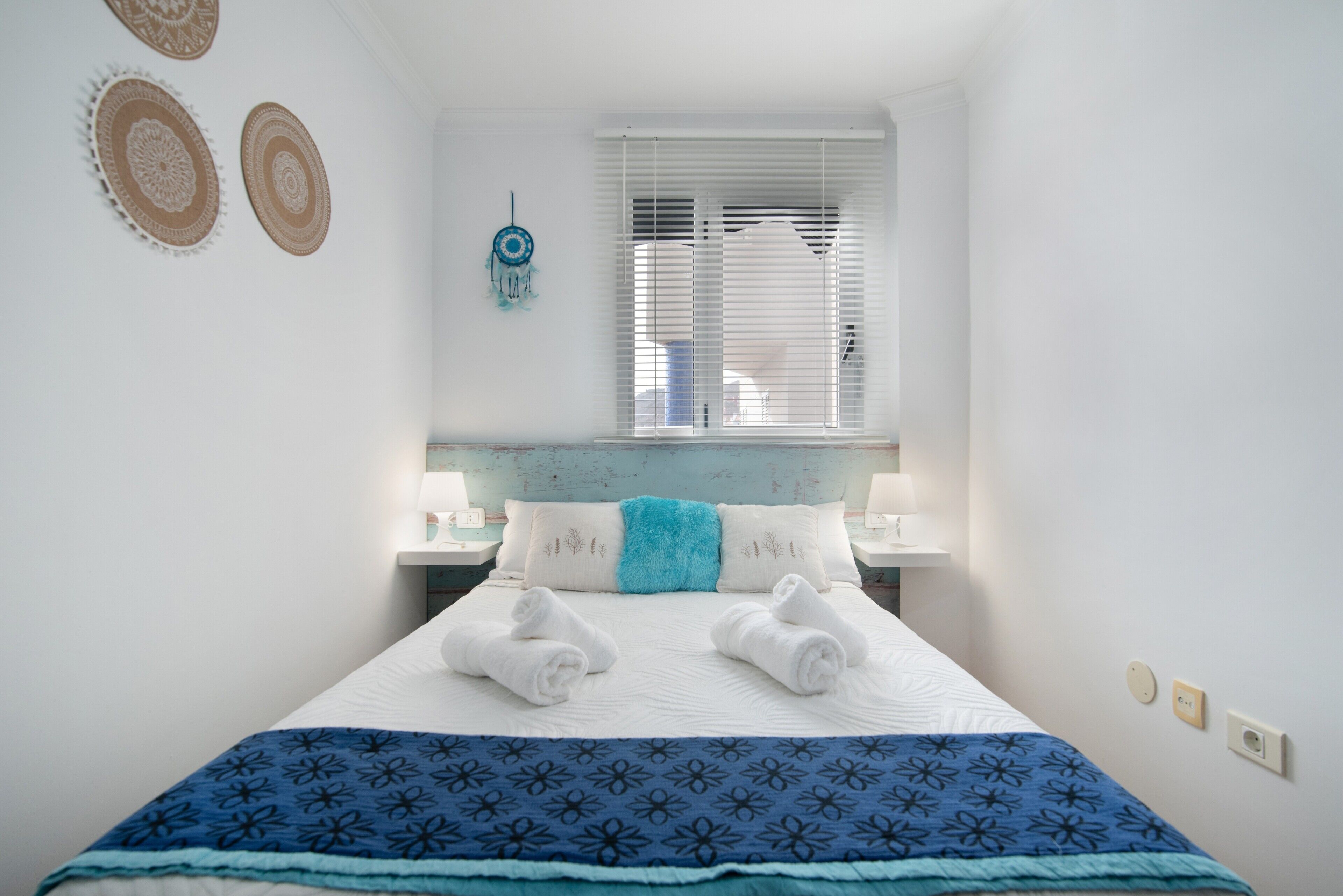 A neatly made bed with towels, a blue blanket, and a wall with decorative plates.