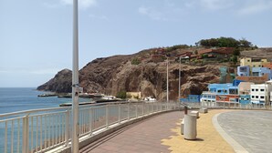 A coastal walkway with a metal railing, a clear sky, and buildings in the background.