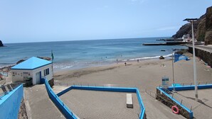 A beach with a lifeguard tower, a small building, and a rocky cliff.