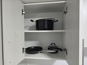 A kitchen cabinet with two shelves, one holding a black frying pan and the other a black pot. - Cozy Urban Retreat  (Calgary)