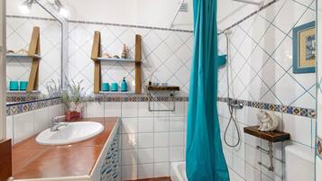 Une salle de bain avec un lavabo, un miroir, des étagères contenant des articles de toilette, un rideau de douche et un tableau encadré au mur.