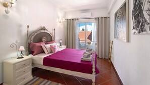 Een slaapkamer met een bed, nachtkastjes, een raam met gordijnen, een schilderij aan de muur en uitzicht op het exterieur.