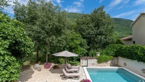 A pool area with a stone patio, lounge chairs, and an umbrella. - Vacation home Gianni by Interhome (Labin)