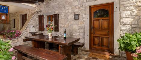 A rustic stone building with a wooden door, a bench, a table, and a welcome mat.